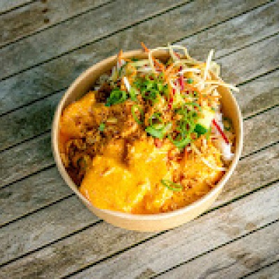 Een kartonnen schaal met daarin een curry gerecht op een houten tafel