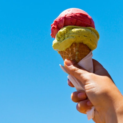 Een hand dat een ijsje met 2 bolletjes vasthoudt tegen een blauwe achtergrond